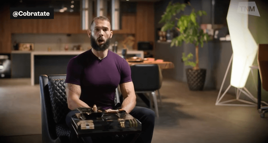 Andrew Tate in a maroon shirt in a warehouse like building